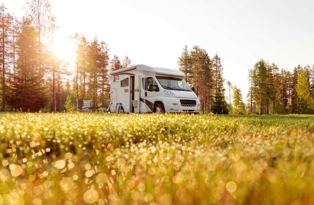Camping-car profilé stationné en pleine nature au lever du soleil, symbole de confort, autonomie et évasion avec Roots Evasion